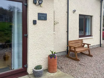 a wooden bench sitting outside of a building at Dalnafeidh Beag - Cottage in Portnacroish