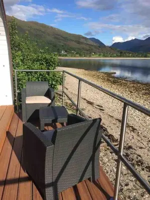 a deck with two chairs and a table next to a body of water at The Boathouse pod in Onich