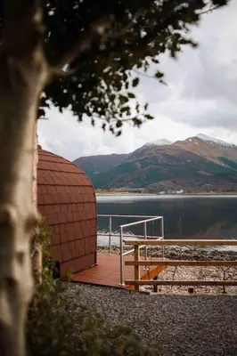 a wooden deck with a view of a lake and mountains at The Boathouse pod in Onich