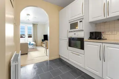 a kitchen with white cabinets and a living room at Modern 1BR flat - free parking + lift in Edinburgh