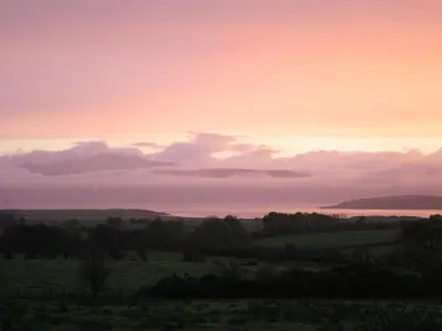a sunset over a field with the ocean in the background at The Coach House at Stewart Hall in Rothesay