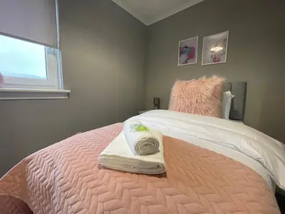 a bedroom with a pink bed with two towels on it at Dunbeth House in Coatbridge