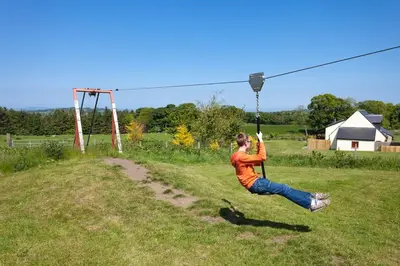 a woman is swinging on a zip line at Appletree Cottage at Williamscraig Holiday Cottages in Linlithgow