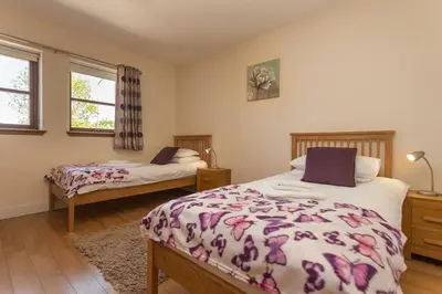 a bedroom with two beds and two windows at Beech Cottage at Williamscraig Holiday Cottages in Linlithgow