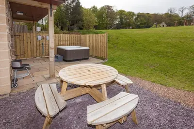 a wooden picnic table and two benches in a yard at Laurel Cottage at Williamscraig Holiday Cottages in Linlithgow