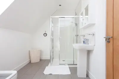 a white bathroom with a shower and a sink at 2 Eden at Williamscraig Holiday Cottages in Linlithgow