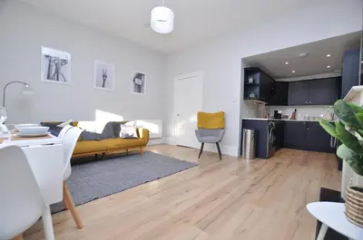 a living room with a yellow couch and a kitchen at The Warren Apartment in Greenock