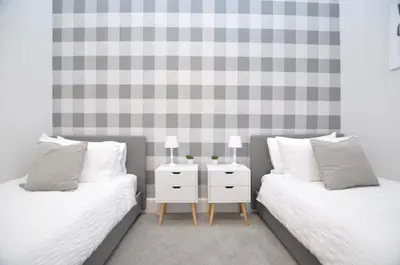 two beds with white pillows and a nightstand between them at The Warren Apartment in Greenock
