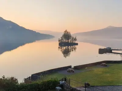 a tree on a island in the middle of a lake at Lochside Apartment in Stronachlachar