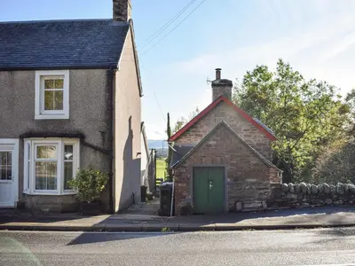 an old stone house with a green door on a street at Daisybank Cottage in Crieff