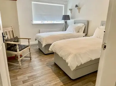 a bedroom with two beds and a chair and a window at Traditional Cottage in West Kilbride Village in Seamill