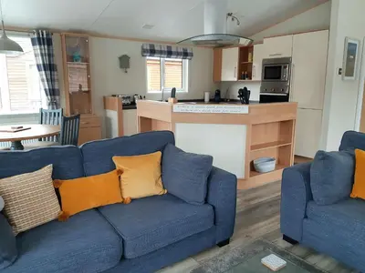 a living room with two blue couches and a kitchen at Sycamore Lodge Auchterarder in Auchterarder