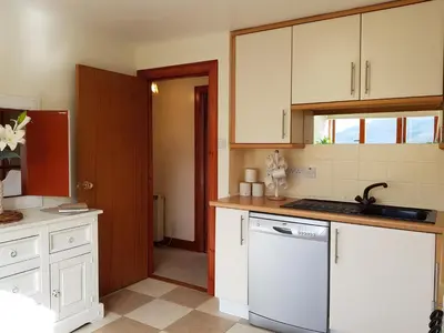 a kitchen with white cabinets and a white dishwasher at The Old Post Office On Loch Tay in Stron-fearnan