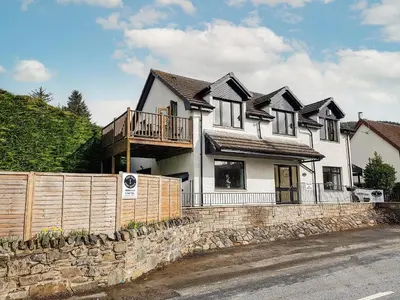 a large white house with a wooden fence at The Old Post Office On Loch Tay in Stron-fearnan