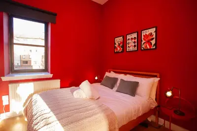 a red bedroom with a bed with white sheets and a window at Glasgow Green Getaway with Free Parking in Glasgow
