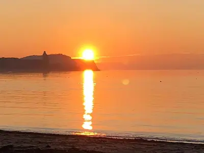 a sunset on the beach with the sun setting over the water at Creathie Cathcart - Georgian Luxury at the beach in Ayr