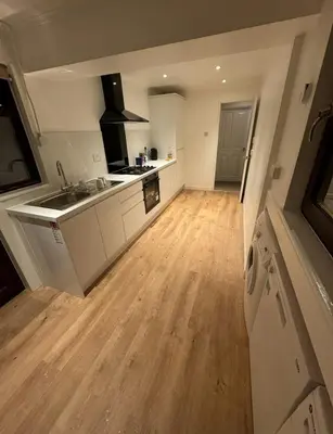 a large kitchen with white cabinets and a wooden floor at 4 Bed House - Sleeps 9 - HotTub - Parking in Beattock
