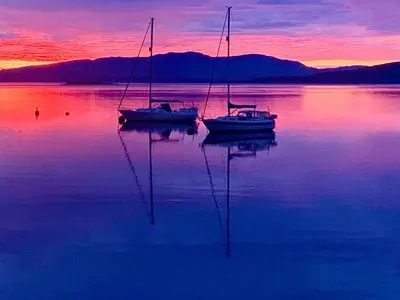 two boats sitting in the water at sunset at Corrie Apartment, Kinlochlaich House in Appin
