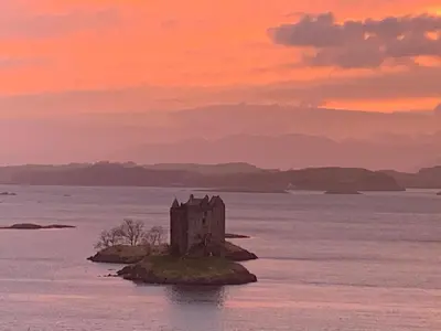 a castle on an island in the water at sunset at Corrie Apartment, Kinlochlaich House in Appin
