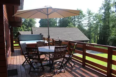 a table and chairs with an umbrella on a deck at Lady Galloway 28 with Hot Tub in Newton Stewart