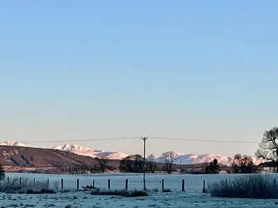 a snowy field with snow covered mountains in the background at Poachers Hut at Keepers Cottage - Hot Tub & Pizza Oven - Trossachs in Port of Menteith