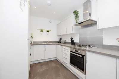 a white kitchen with white cabinets and a stove at Stylish 3BR Home with Garden & Free Parking - Near O2 Academy & City Centre in Glasgow