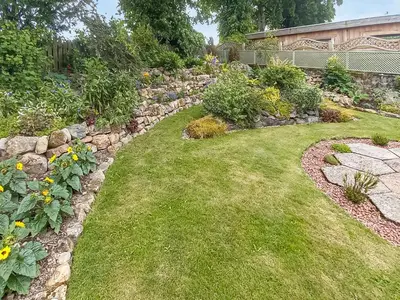 a garden with a stone retaining wall and a lawn at The Shieling in Biggar