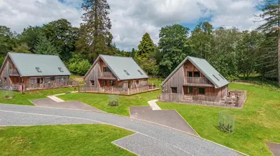three wooden houses on a grassy field with a road at Lord Galloway 33 with Hot Tub in Newton Stewart