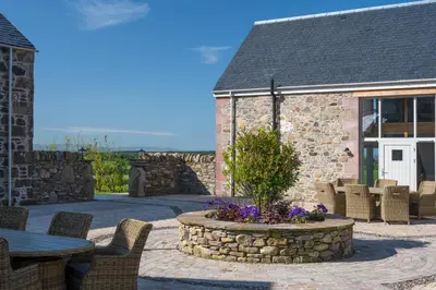 a patio with a table and chairs and a building at Kipney Farmhouse with hot tub in Perth
