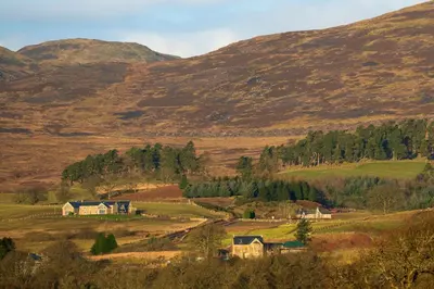 a farm in a field with mountains in the background at Oystercatcher - Converted luxury steading in Perth