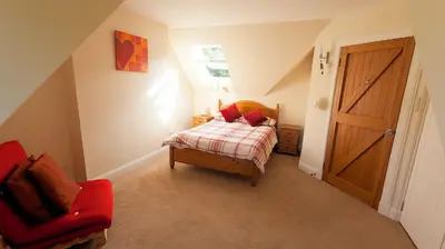 a small bedroom with a bed and a red chair at The Byre in Strathyre