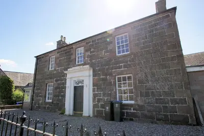 an old brick building with a door and a fence at Comrie Old Schoolhouse in Comrie