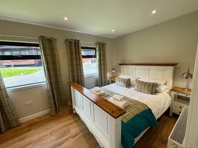 a bedroom with a large bed and two windows at Bluebell Lodge 11 with Hot Tub in Newton Stewart