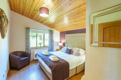 a bedroom with a bed and a chair and a mirror at Laurel Lodge 6 with Hot Tub in Newton Stewart
