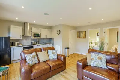 a living room with two leather chairs and a kitchen at Conifer Lodge 8 with Hot Tub in Newton Stewart
