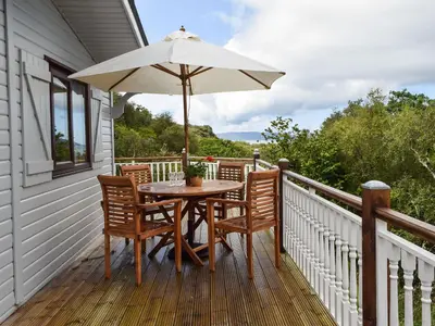 a table and chairs on a deck with an umbrella at Catkin Lodge - Uk39646 in Lunga