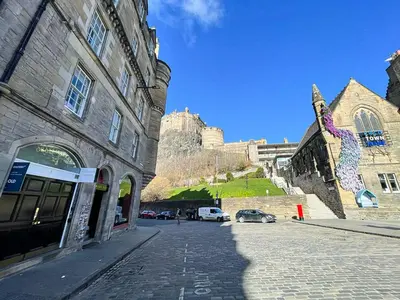 a cobblestone street next to a building with a castle in the background at Snug Studio on The Grassmarket, 5mins from Castle in Edinburgh