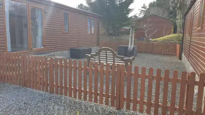 a wooden fence with a bench in front of a house at Red Squirrel Lodge in Auchterarder