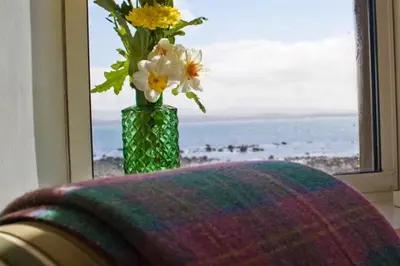 a vase with flowers sitting on a table near a window at Loch Gorm House in Bruichladdich