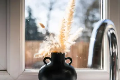 a black vase with feathers in it sitting in a window at Quirky, Family Home in Glasgow in Cardonald