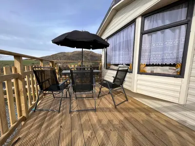 a patio with chairs and an umbrella on a deck at JS Holidays The Westmorland Lagganhouse in Ballantrae