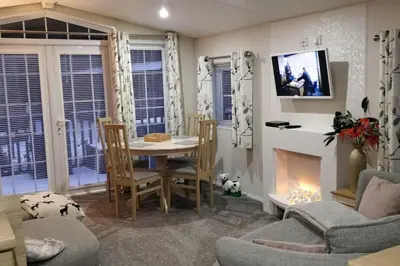 a living room with a table and chairs and a fireplace at Poppy Lodge Glendevon Scotland in Glendevon
