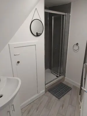 a bathroom with a shower and a sink and a mirror at Black Cat Cottage in Moffat
