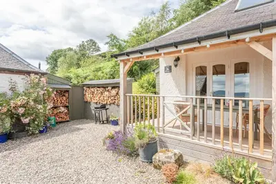 a cottage with a deck and a patio at The Stable - cottage with a spectacular lake view in Port of Menteith