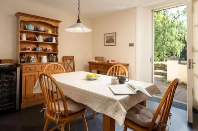 a dining room with a table and chairs and a kitchen at Mossfennan House in Drummelzier