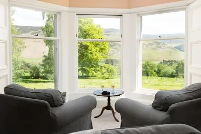 a living room with two couches and a table and windows at Mossfennan House in Drummelzier