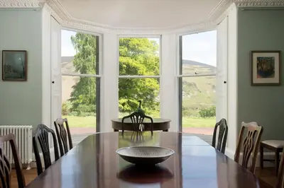 a dining room with a table and a large window at Mossfennan House & Annexe in Drummelzier
