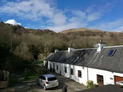 a white house with a car parked in front of it at Historic cottage next to loch lomond Luss in Alexandria