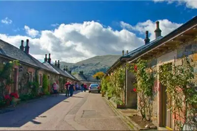 a street with buildings and people walking down the street at Historic cottage next to loch lomond Luss in Alexandria