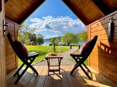 a porch with two chairs and a table with wine glasses at Seal Cove Cabin - Luxury Glamping in Cairndow